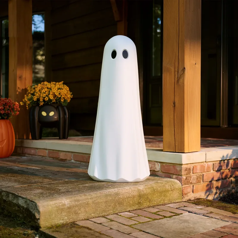 White ghost figure displayed on a front porch beside autumn planters