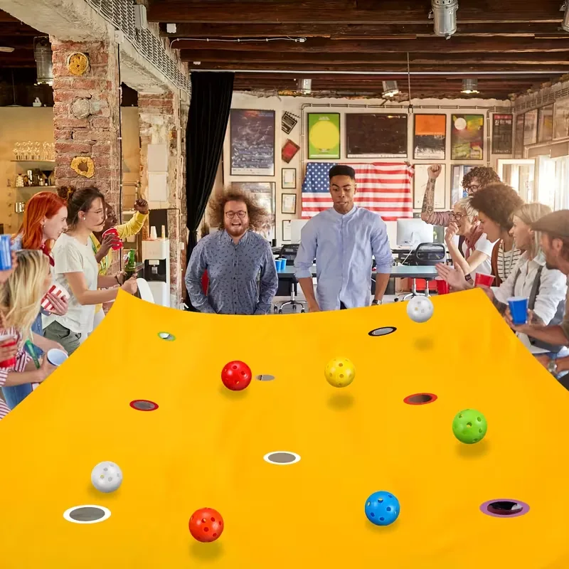 Group playing a yellow multi-hole tarp game with colorful balls indoors